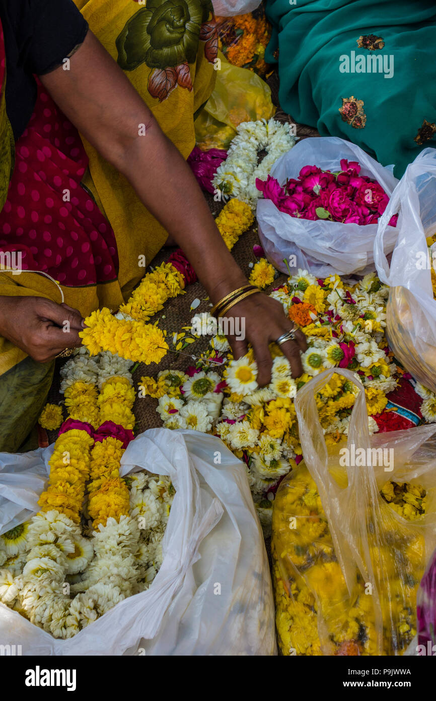 Donna indiana rendendo tradizionali di ghirlande di fiori in un mercato in stallo la Vecchia Delhi, Delhi, India Foto Stock