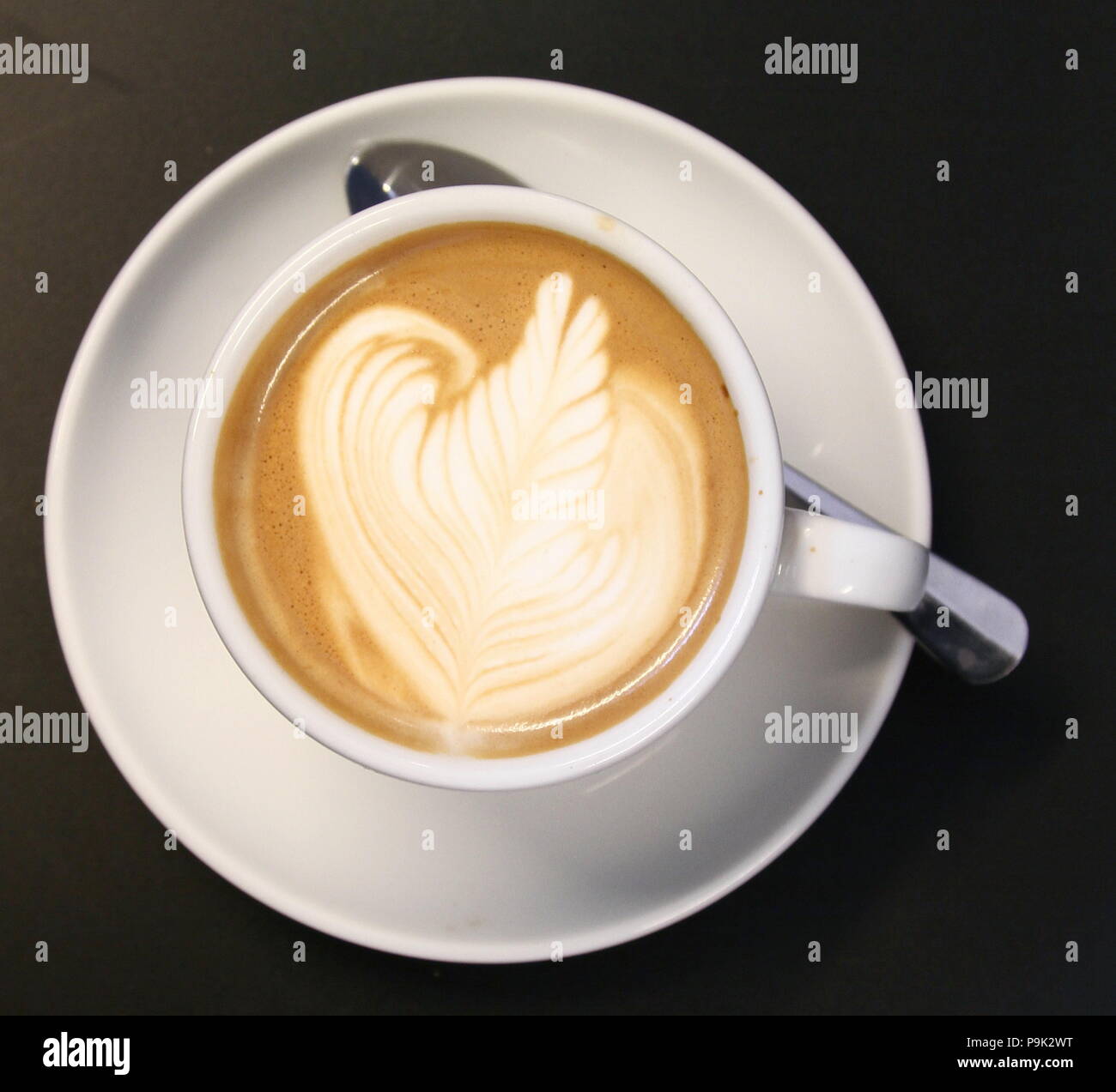 Un caffè in una tazza bianca con tazza su bianco piattino e cucchiaio d'argento sul piattino. Esperto Barista ha decorato la superficie della schiuma . Credito foto Russell Moore. Foto Stock