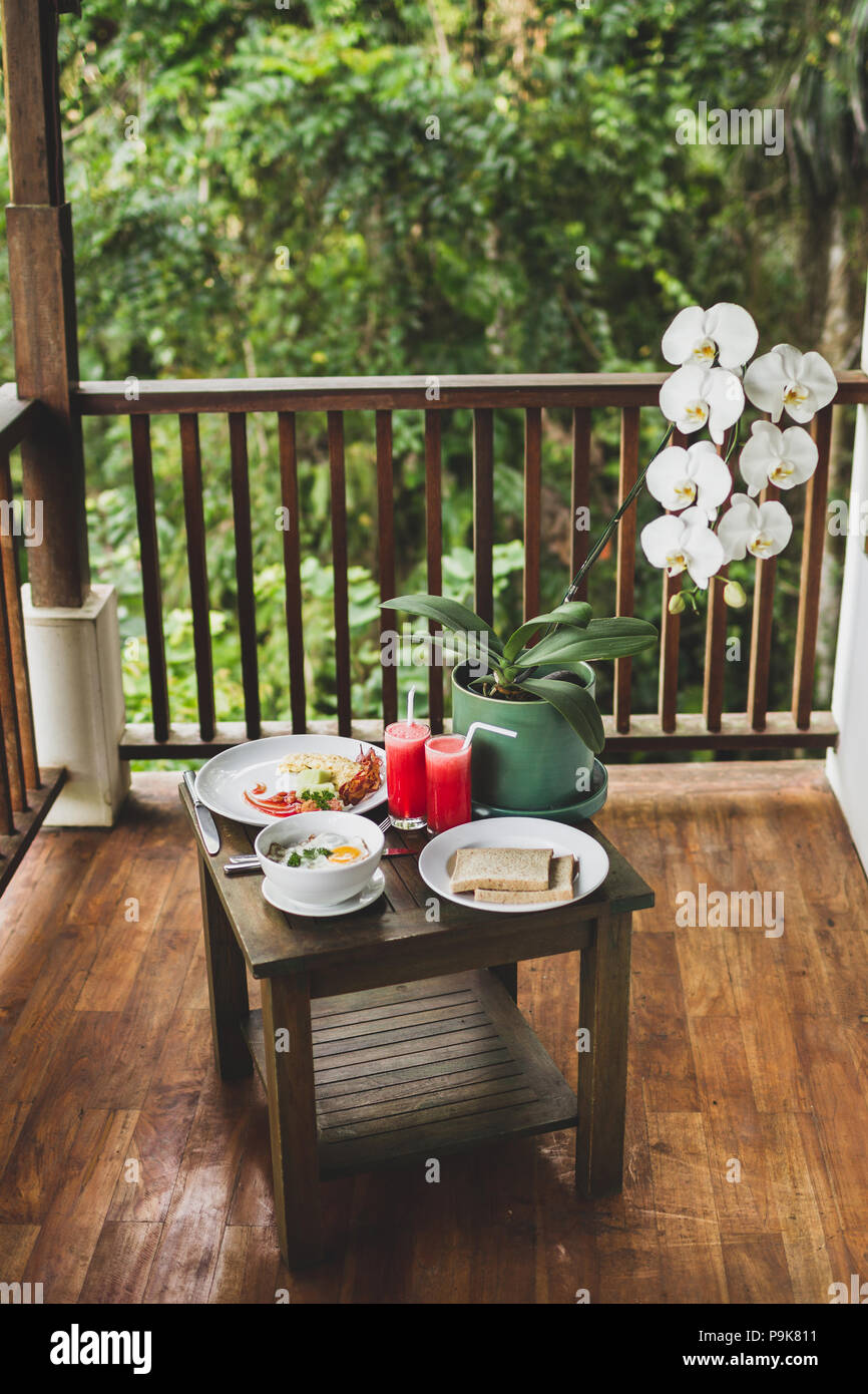 La prima colazione all'aperto sulla terrazza in legno con vista Giungla Uova fresche di anguria succo di frutta e di fiori di orchidea sul tavolo Foto Stock