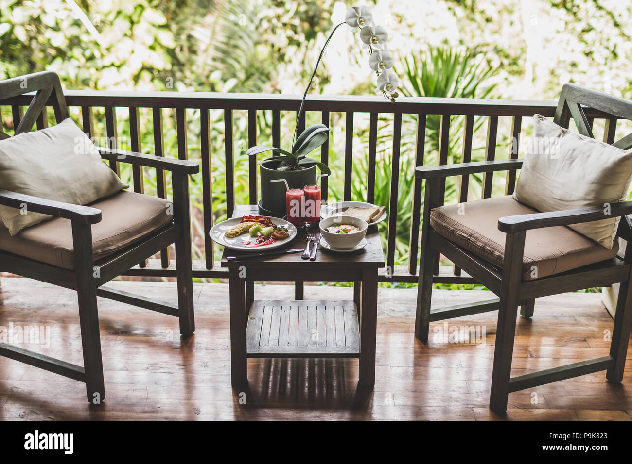 La prima colazione all'aperto sulla terrazza in legno con vista Giungla Uova fresche di anguria succo di frutta e di fiori di orchidea sul tavolo Foto Stock