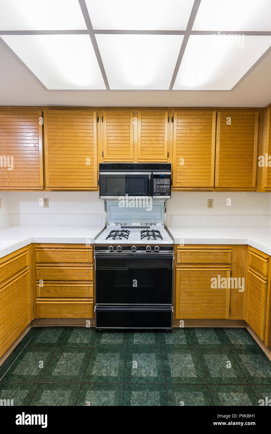 Condominio vecchia cucina vista verticale con rovere cabinetes, tile countertops, fornello a gas e pavimento in verde. Invariata dal 1988. Foto Stock