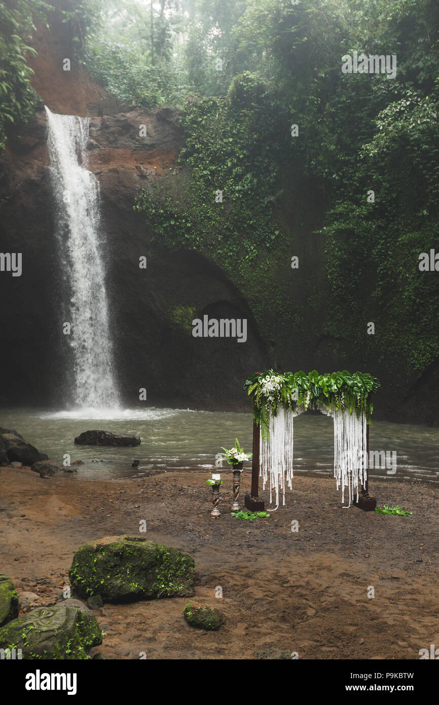 Tropical cerimonia di nozze con vista cascata. Arco bianco decorato con giungla verde lascia monstera e fern Foto Stock