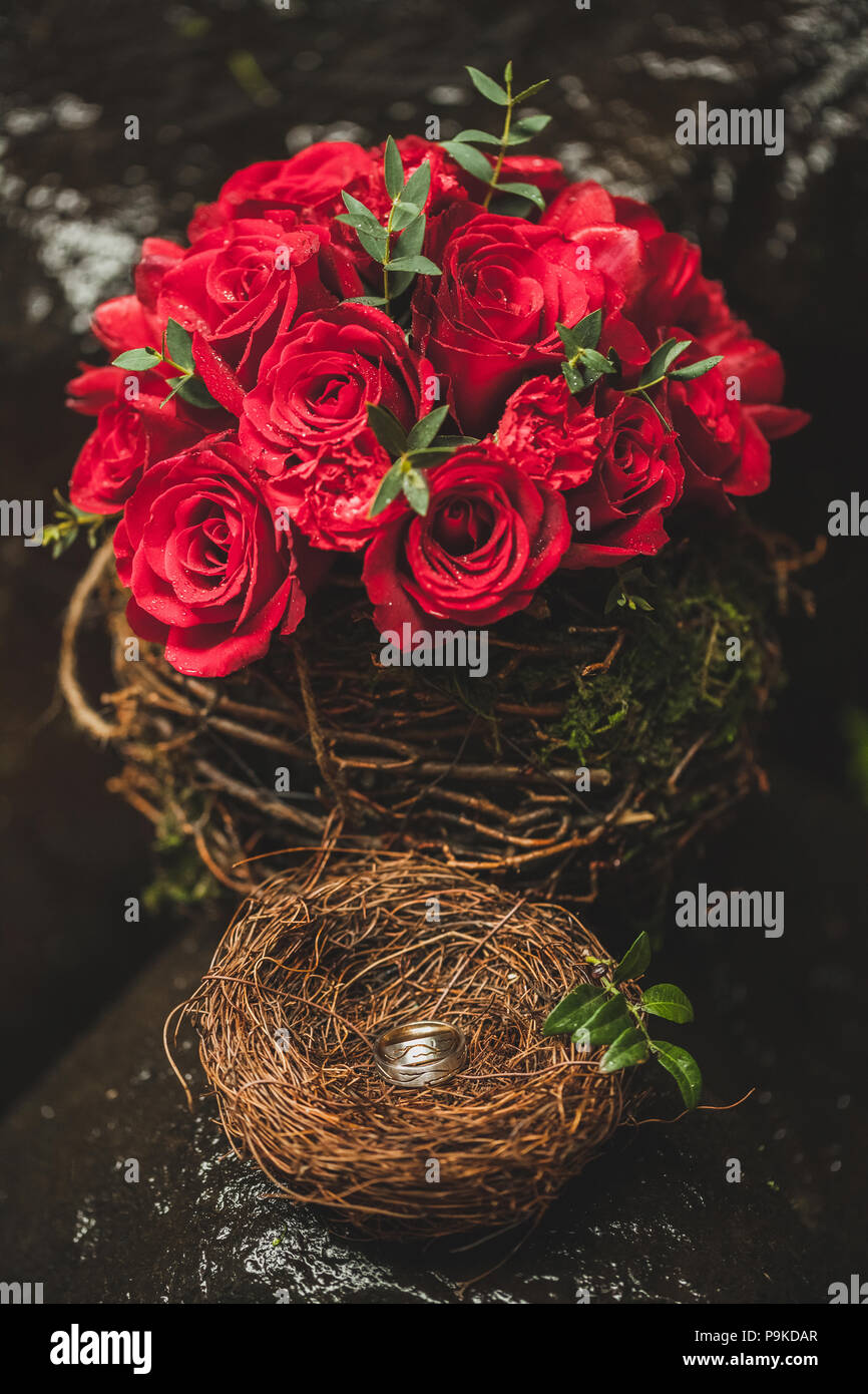 Due golden gli anelli di nozze in vimini nido fatti a mano con red bouquet di rose Foto Stock