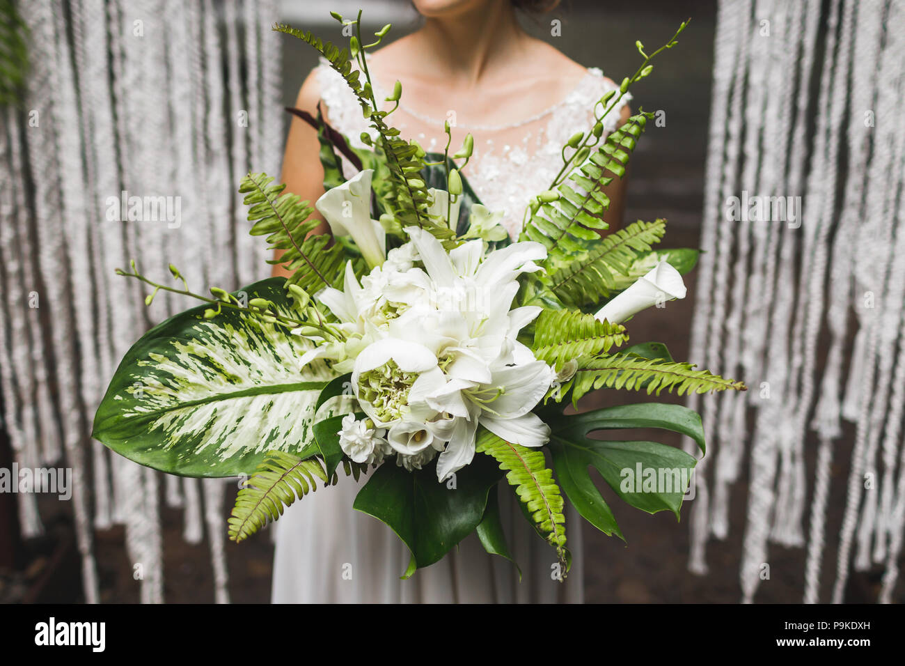 Sposa tenendo in mano un enorme bouquet di verde con foglie tropicali e fiori Foto Stock