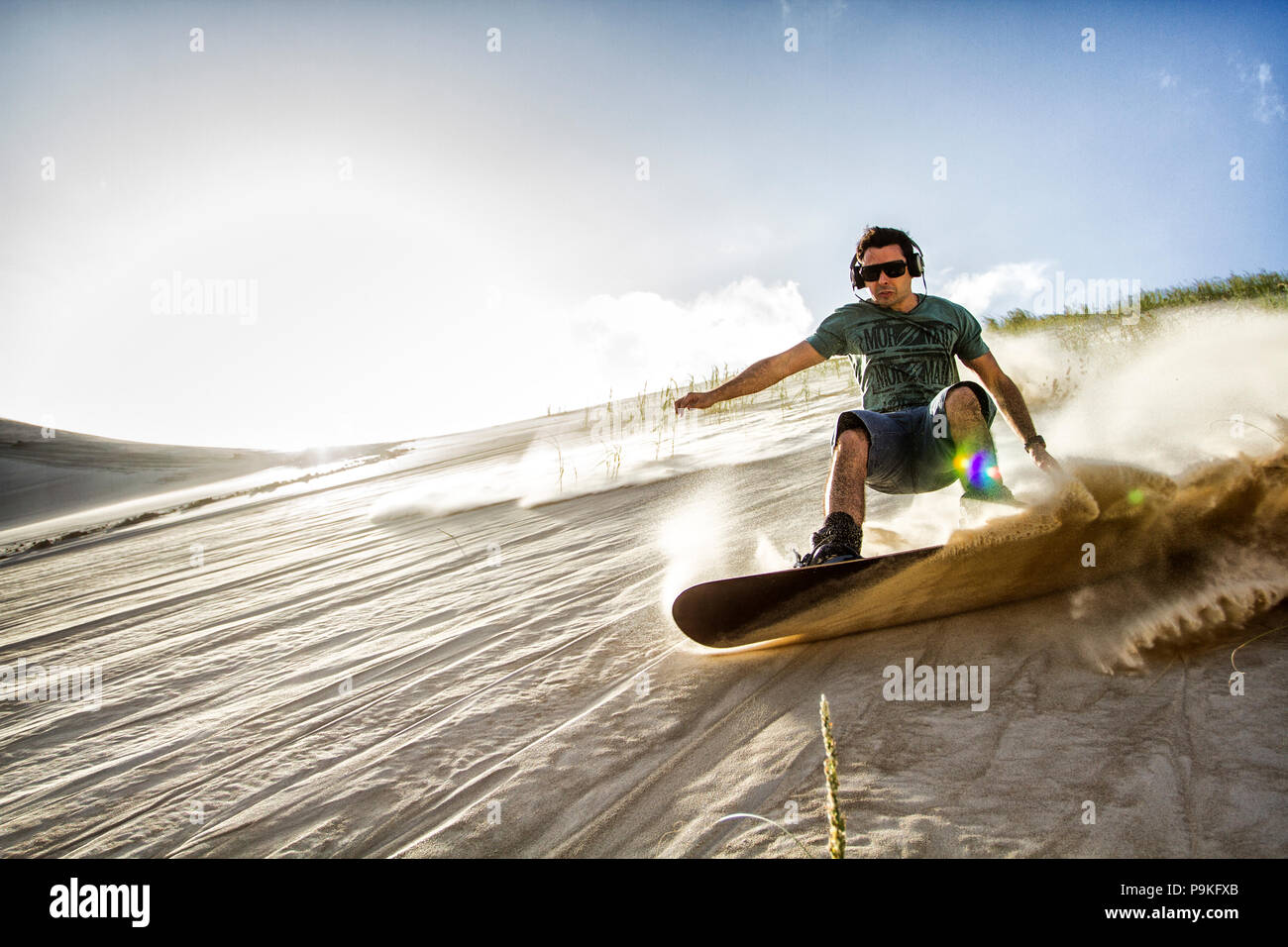 Sandboarding uomo e indossa le cuffie sulle dune della spiaggia Ribanceira. Imbituba, Santa Catarina, Brasile. Foto Stock