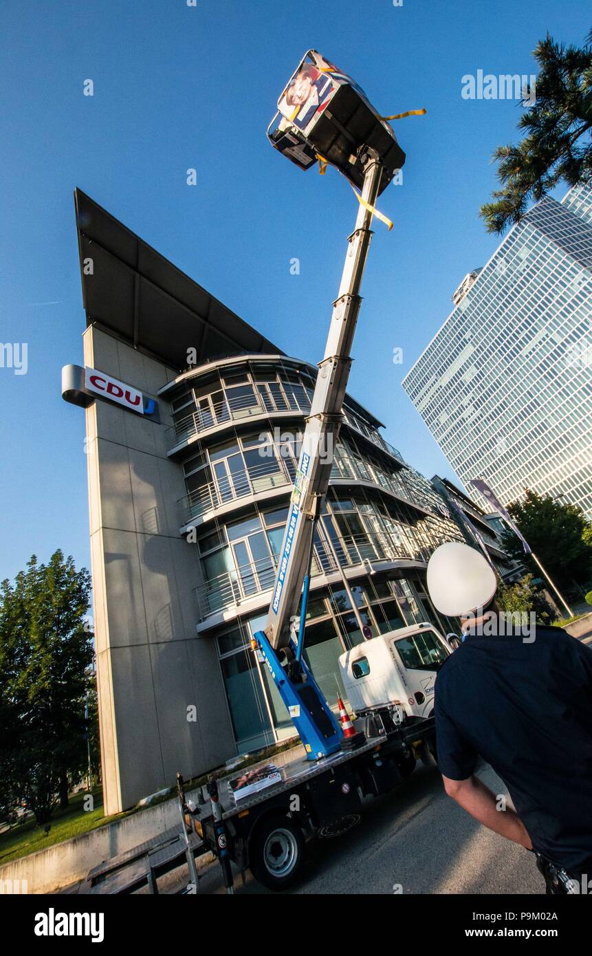 Monaco di Baviera, Germania. 18 Luglio, 2018. Un ufficio di polizia guarda un acciaio zincato troupe stati nella gru dopo aver appeso il CDU segno oltre la CSU del logo. La politica performing arts troupe das Zentrum fuer Politische Schoenheit (Centro di Bellezza politico) ha organizzato una azione politica presso la sede della CSU bavarese partito, messa a terra del CDU partito in Baviera come forma di protesta. Durante la dimostrazione, il gruppo ha portato in una gru mobile e coperto la CSU il segno con quello della CDU. Esso ha preso la polizia di scomposizione per più di trenta minuti per portare la troupe stati verso il basso, durante il quale t Foto Stock