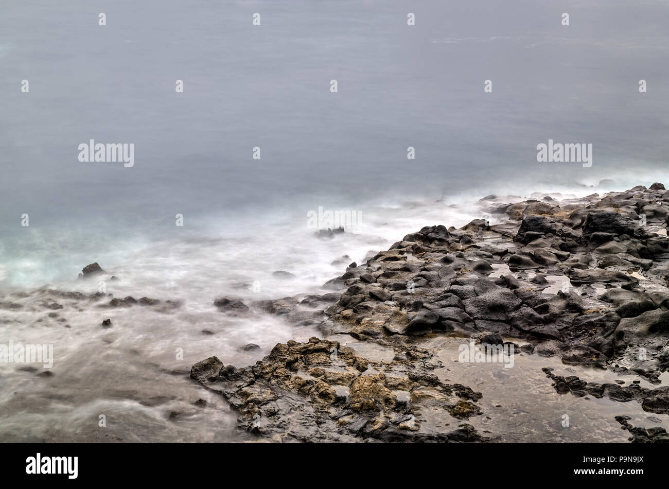 Una lunga esposizione fotografia di un roccioso riva del mare con spiaggia, pietre e le piscine incontro onde spettrale dell'oceano. Concetto di pace di serenità. Copia dello spazio. Foto Stock