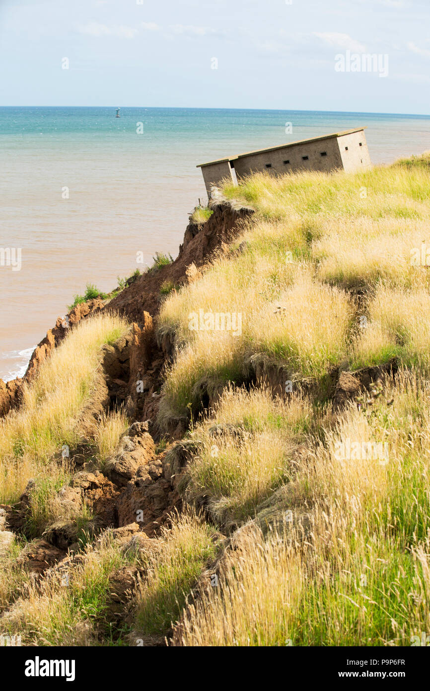 Una seconda guerra mondiale lookout post appoggiata in maniera allarmante e circa per capovolgere sul bordo della scogliera nei pressi di Aldbrough Yorkshires sulla costa est, UK. La costa è composta da morbide argille di boulder, molto vulnerabili alla erosione costiera. Questo tratto di costa è stata erodendo sin dai tempi dei romani, con molti villaggi aventi scompare in mare, ed è il più veloce erodendo la costa in Europa. Il cambiamento climatico è accelerare l'erosione, con innalzamento del livello del mare, aumentato le tempeste e aumento della pioggia pesante eventi, tutti di fare la loro parte. Foto Stock