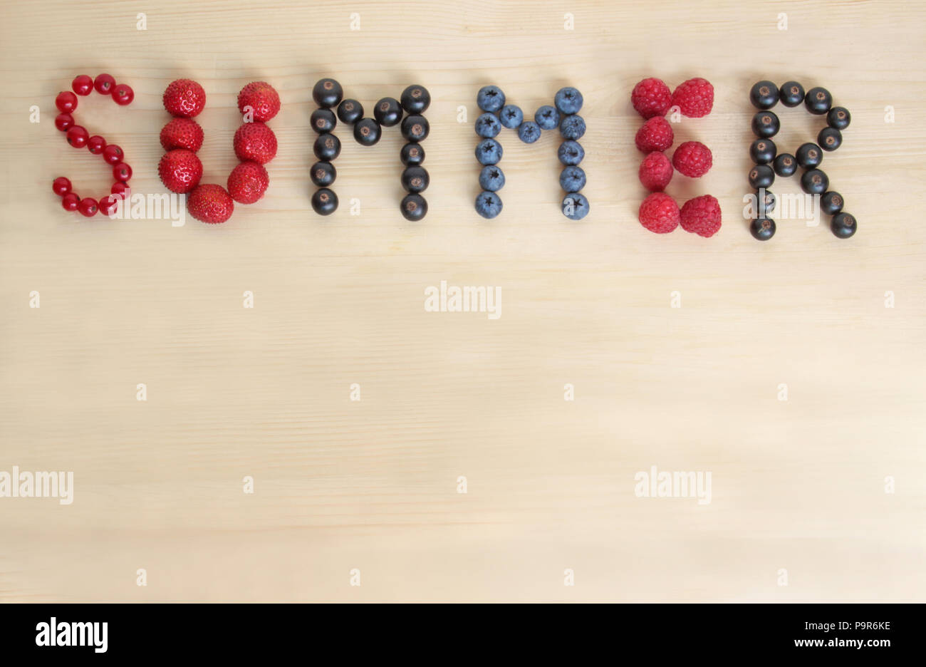 La parola 'Summer' prevista con vari frutti di bosco su un tavolo di legno Foto Stock
