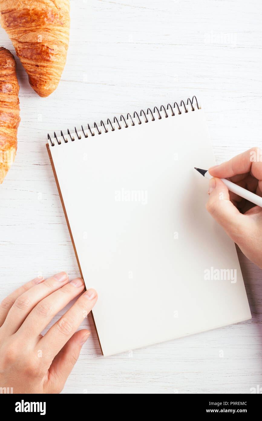 La donna è la scrittura a mano in notebook bianco su un tavolo di legno. Luogo di lavoro e il concetto di pianificazione, mattina tempo, vista dall'alto. Foto Stock