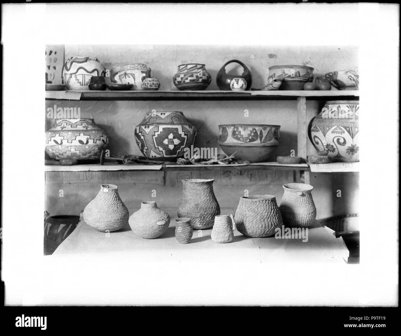 . Inglese: raccolta di circa 25 pezzi di Indiani Pueblo pottery, ca.1900 fotografia di una collezione di circa 25 pezzi di Indiani Pueblo pottery, ca.1900. La ceramica può essere visto visualizzata su tre ripiani o livelli. La parte superiore e inferiore di righe di ceramica sono di origine antica, mentre i pezzi nella fila centrale sono moderni. La ceramica è dipinto e assume una varietà di forme e dimensioni. Alcune etichette sono visibili su alcuni dei pezzi. I sette pezzi sul livello inferiore sono testurizzati approssimativamente simili cestelli. Le punte delle frecce montato su una scheda sono visualizzati sul ripiano più in alto a sinistra. Parti di un giornale(?) ha Foto Stock