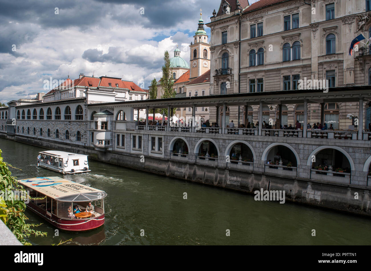 La Slovenia, Europa: egli skyline del centro di Ljubljana con un imbarcazione turistica crociera sul fiume Ljubljanica, conosciuta nel Medioevo come Ljubija Foto Stock