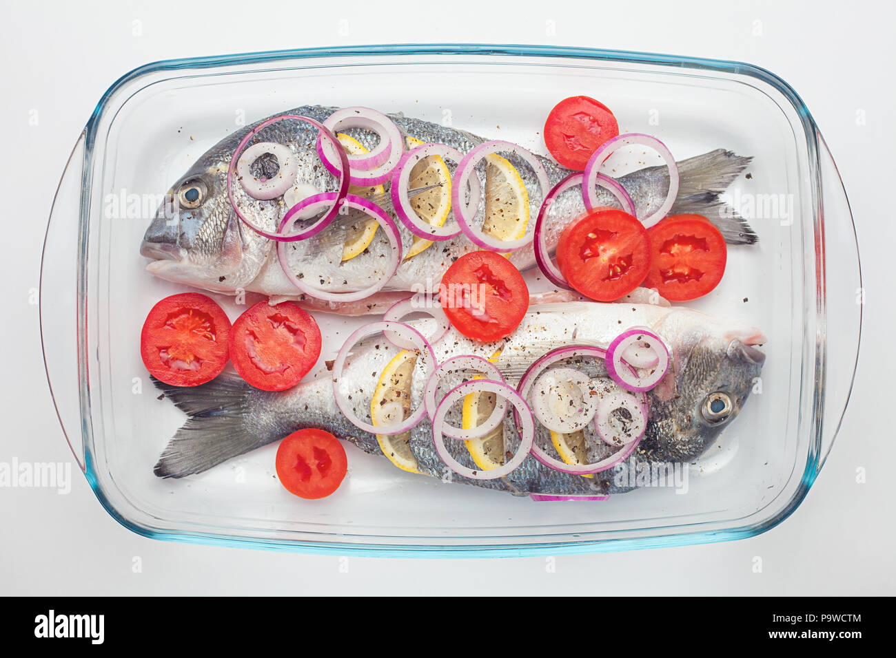 Materie dorado pesce crudo con limone e verdure, pomodori, cipolle, spezie su un piatto di vetro Foto Stock