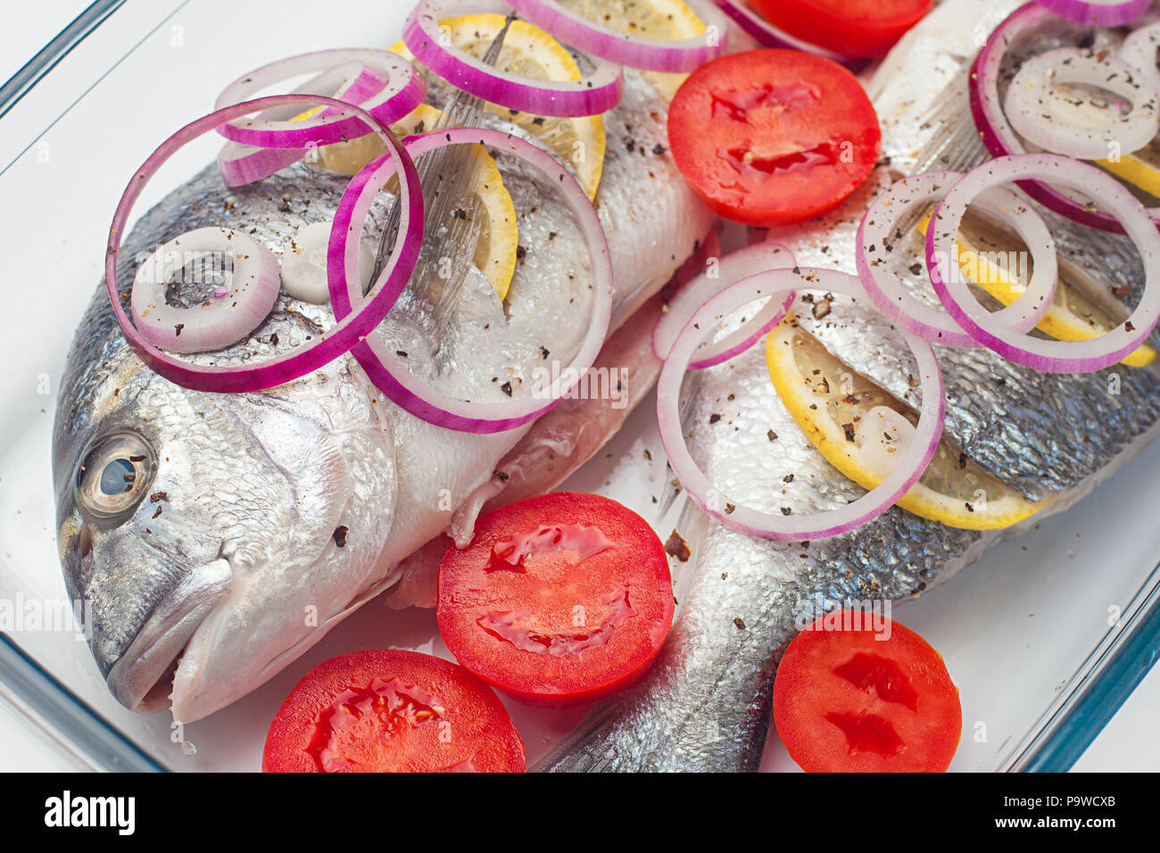 Materie dorado pesce crudo con limone e verdure, pomodori, cipolle, spezie su un piatto di vetro Foto Stock