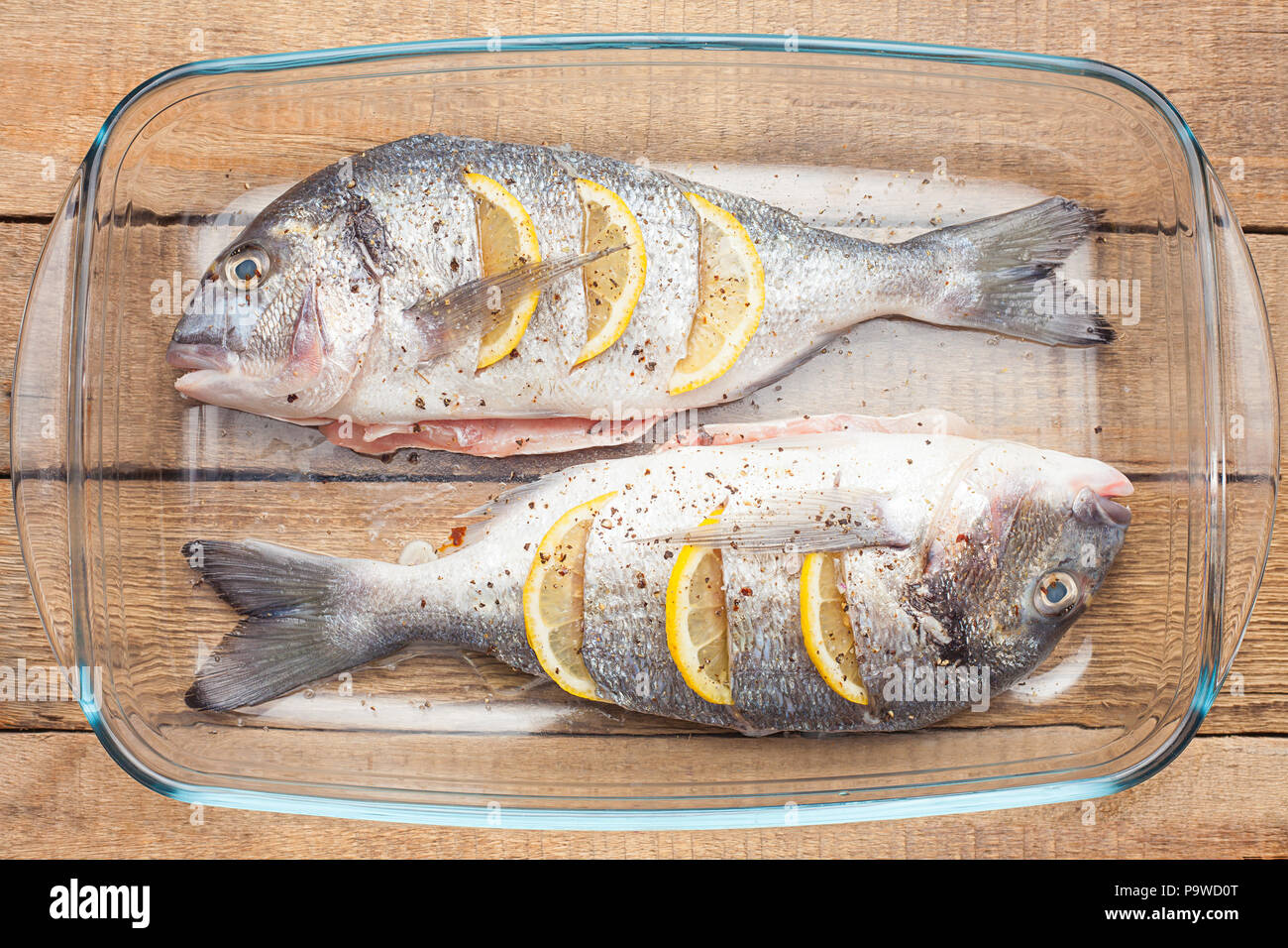 Materie dorado pesce crudo con limone e verdure, pomodori, cipolle, spezie su un piatto di vetro Foto Stock