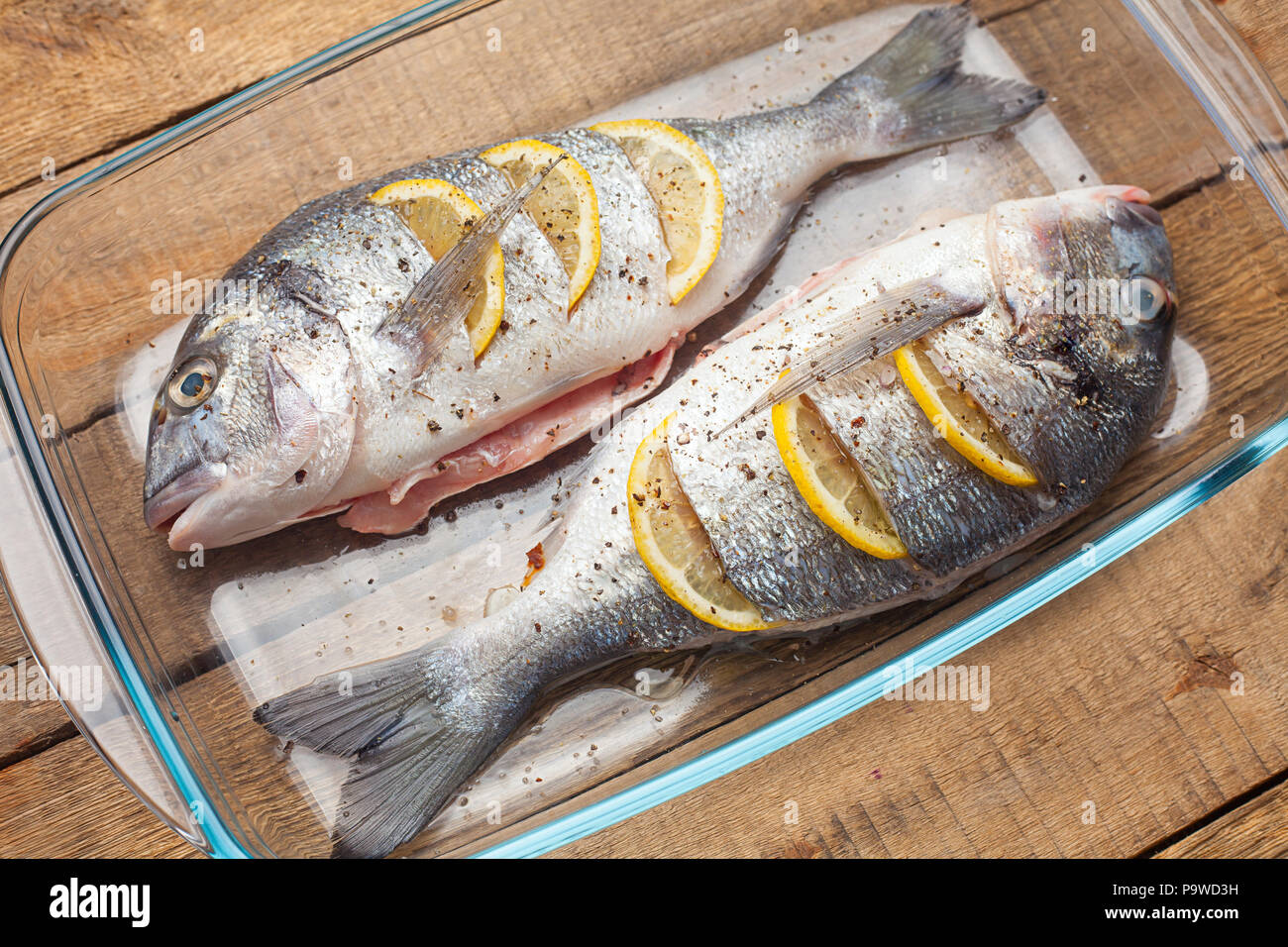 Materie dorado pesce crudo con limone e verdure, pomodori, cipolle, spezie su un piatto di vetro Foto Stock