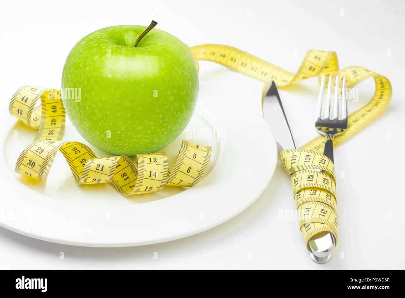 Concetto di dieta, mela verde su una piastra bianca, gialla rubinetto di misurazione Foto Stock