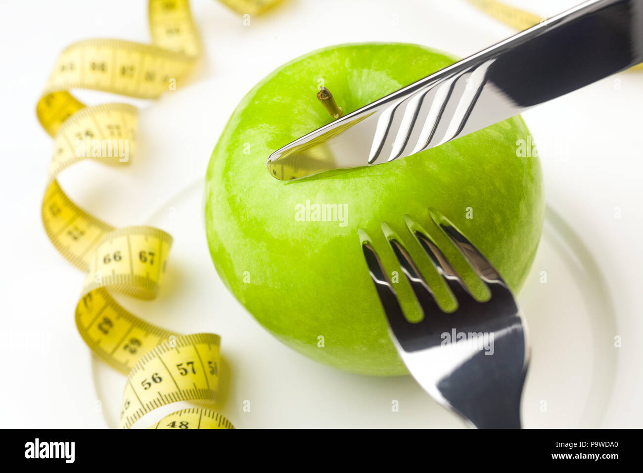 Concetto di dieta, mela verde su una piastra bianca, gialla rubinetto di misurazione Foto Stock