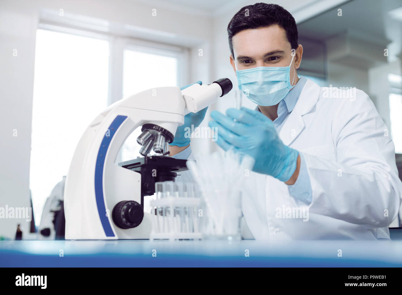 Laboratorio biologico. Bello smart biologo giovane seduto vicino al microscopio e facendo la ricerca durante il lavoro nel laboratorio biologico Foto Stock