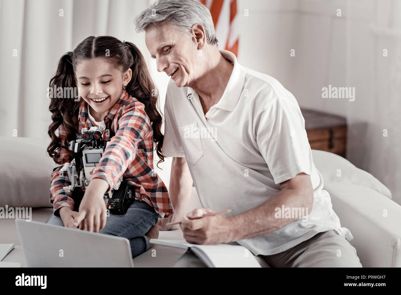 Nuove scoperte giornalmente. Maestoso sbadato il nonno godendo del tempo con graziosi sorridente ragazza che puntare il dito sul monitor sul divano Foto Stock