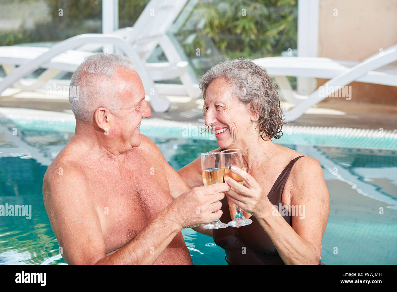 Coppia senior celebrando con un bicchiere di vino frizzante in piscina presso la spa hotel Foto Stock