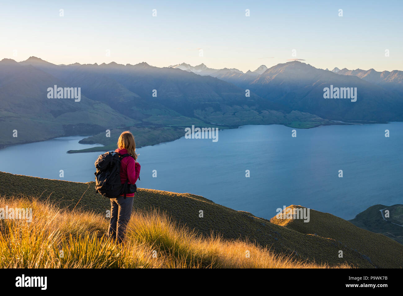 Escursionista femmina a picco istmo, il lago Wanaka e panorama di montagna a pressione atmosferica della luce della sera, Otago, Isola del Sud, Nuova Zelanda Foto Stock