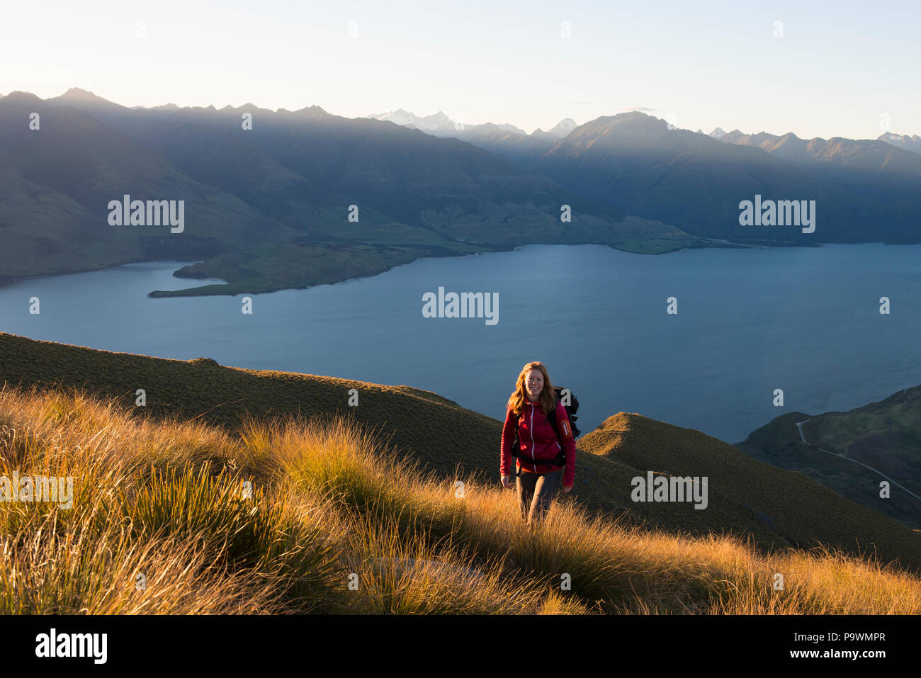 Escursionista femmina a picco istmo, il lago Wanaka e panorama di montagna a pressione atmosferica della luce della sera, Otago, Isola del Sud, Nuova Zelanda Foto Stock