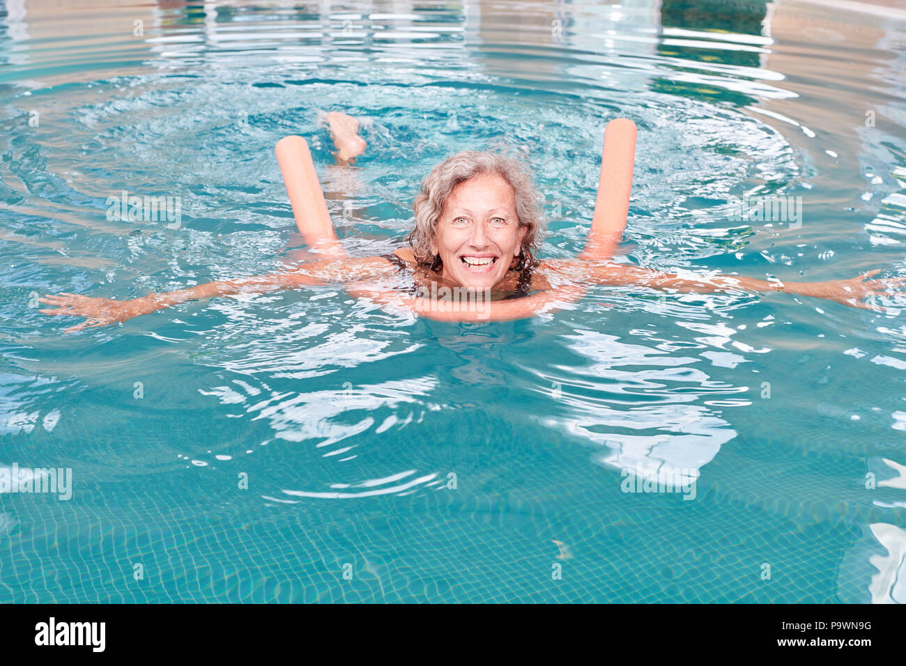 Vitale donna senior in piscina con nuoto aiuto in rehab facendo aerobica in acqua Foto Stock