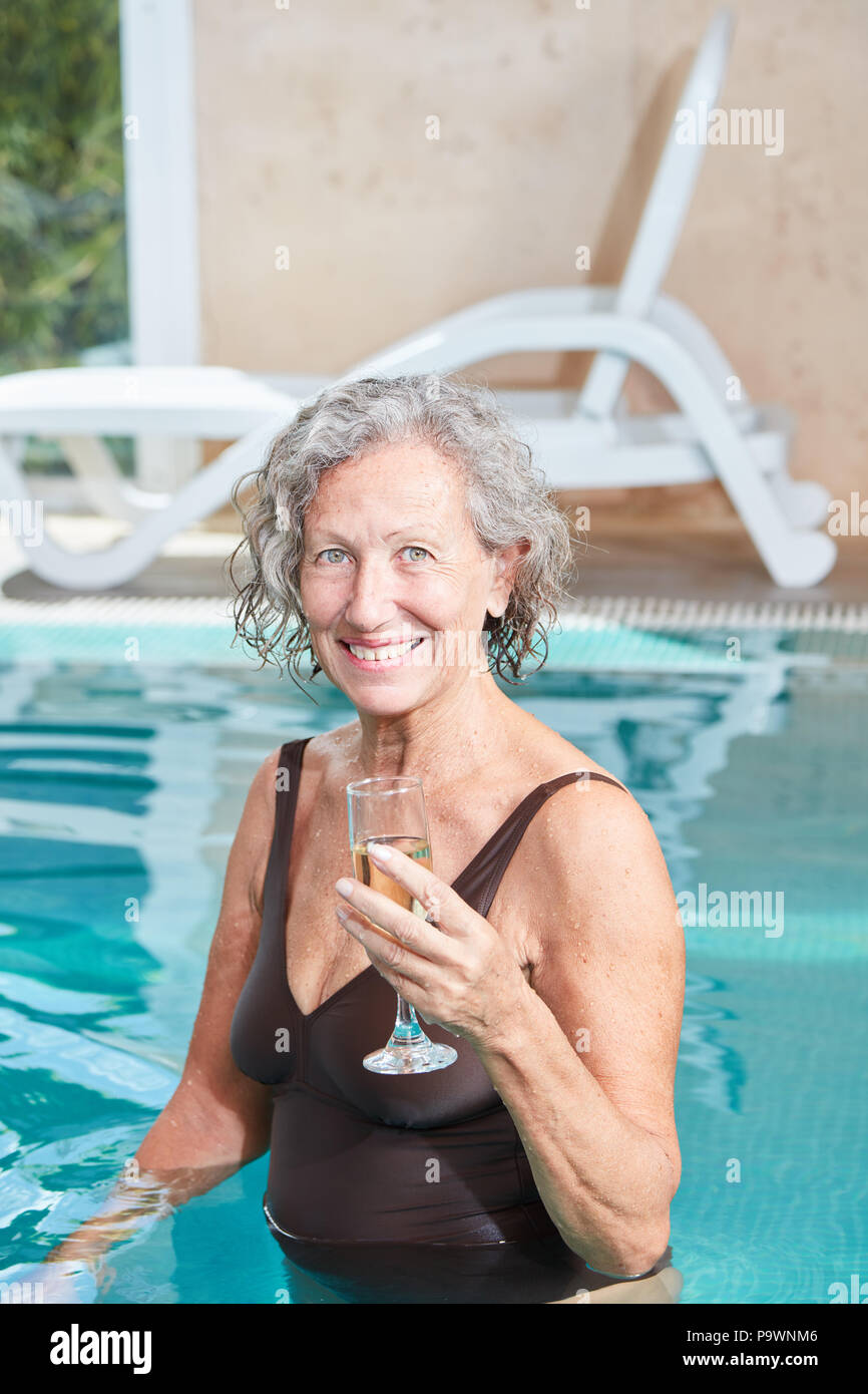 Felice donna senior in piscina con un bicchiere di champagne su una vacanza termale Foto Stock