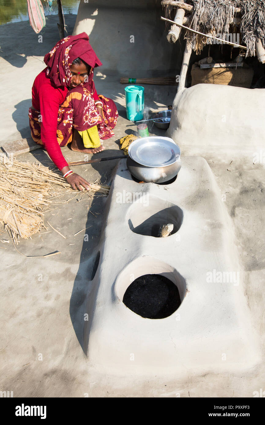 Una donna agricoltore di sussistenza per la cottura su un tradizionale forno di argilla, utilizzando gli steli di riso come biocarburante nel Sundarbans, Gange, Delta, India. La zona è molto basso e vulnerabile di innalzamento del livello del mare. Tutte le parti del raccolto di riso sono usati e gli abitanti del villaggio la vita è molto autosufficiente, con una piccola impronta di carbonio. Foto Stock