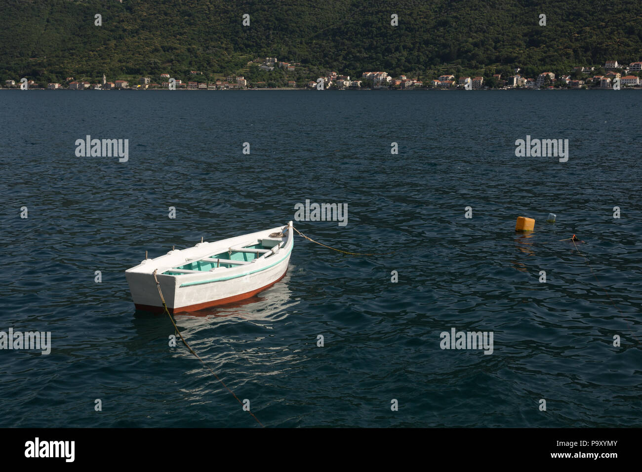 Unico piccolo isolato piuttosto bianco, verde e rosso a remi in legno barca ancorata e galleggiante nel mare Adriatico presso la Baia di Kotor, Perast, Montenegro Foto Stock