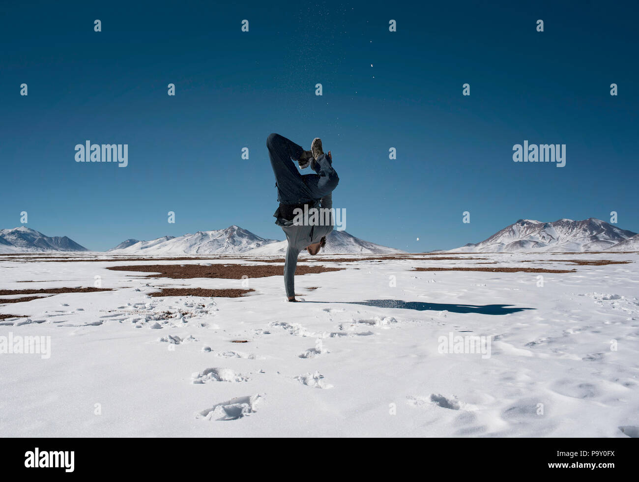 Ragazzo in piedi su una mano nella neve (Chiguana deserto di vulcani in background), Bolivia. Foto Stock