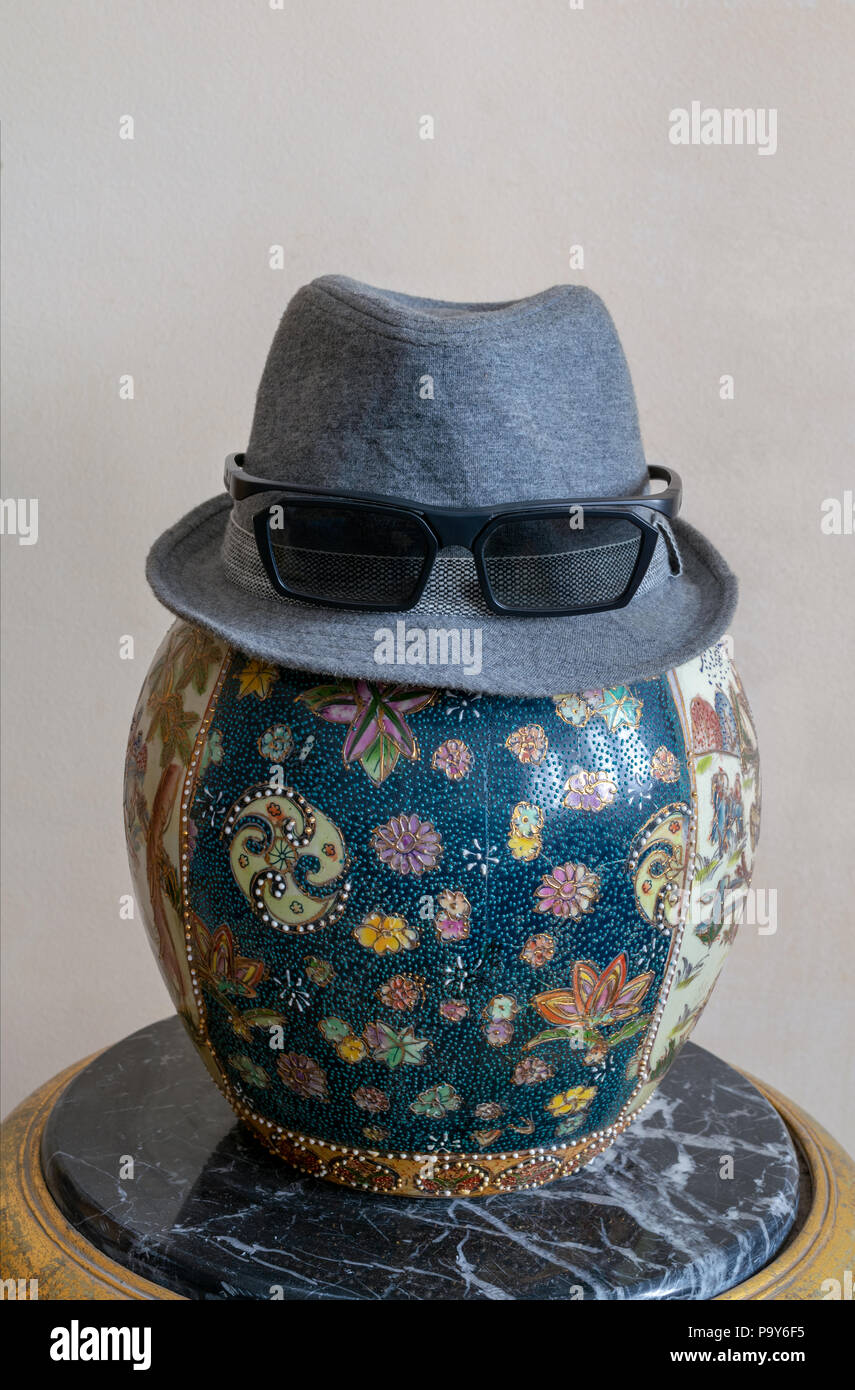 Grigio trilby hat indossando occhiali da sole su antiche decorate in ceramica cinese vaso jar più antico in marmo nero tabella Foto Stock