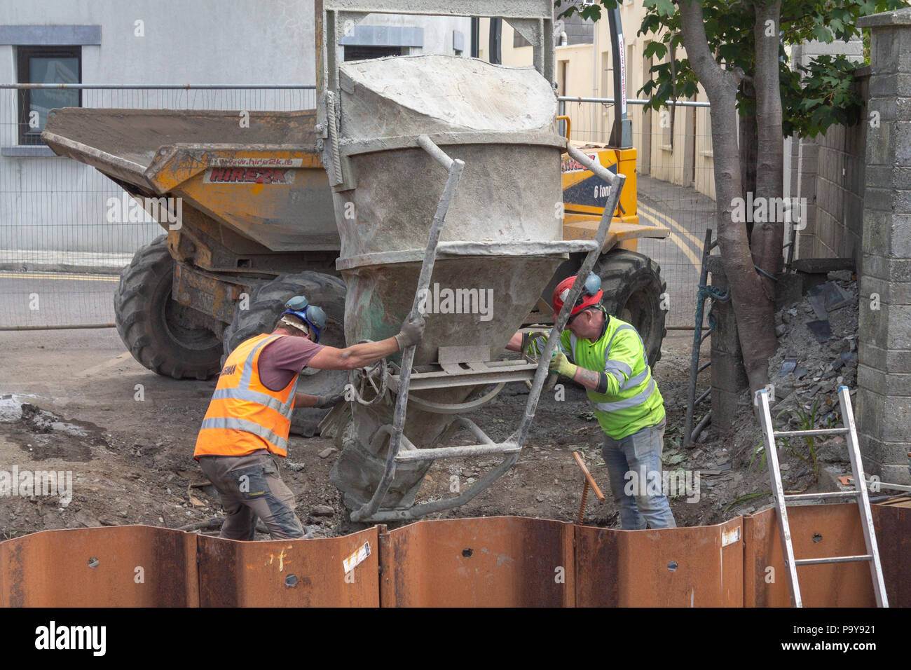 Costruttori la colata di cemento in cassaforma metallica da una tramoggia ribaltabile a mediante la gru. Foto Stock