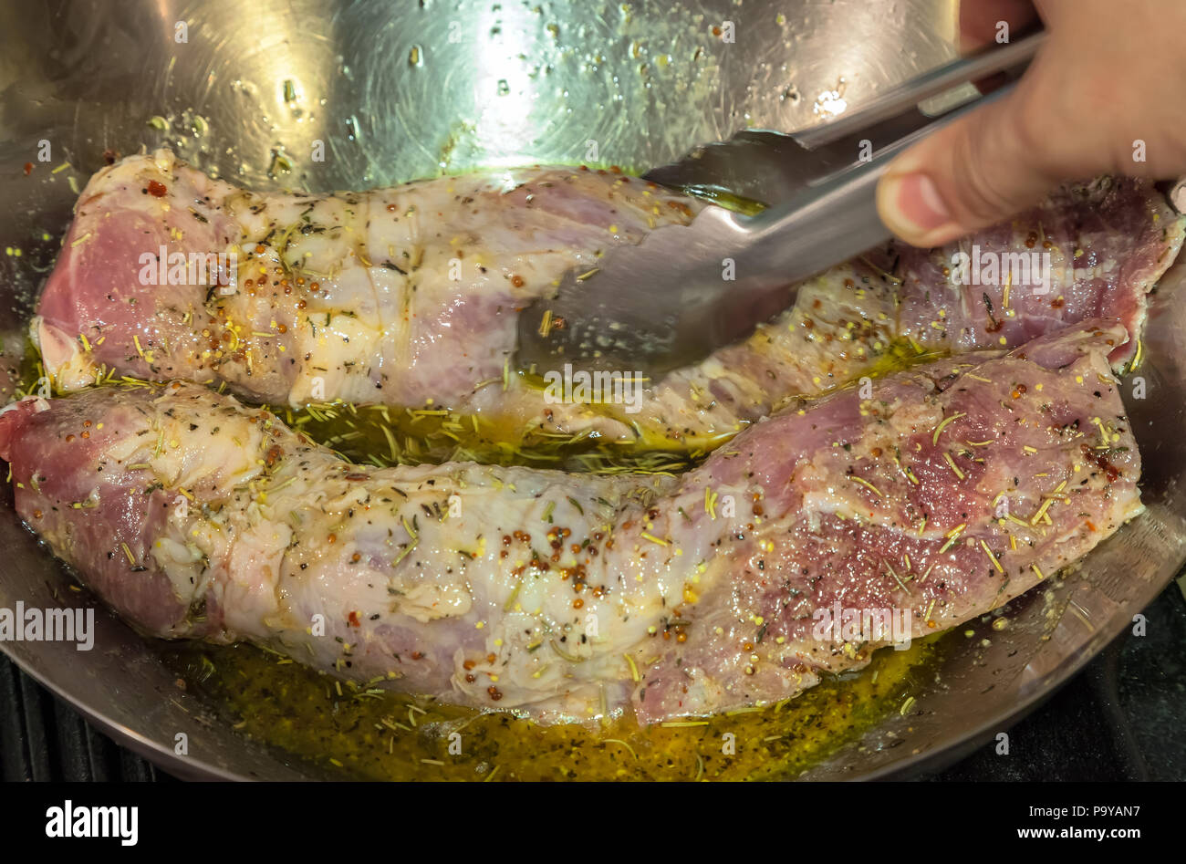 Filetto di maiale sono state condendo con erbe aromatiche e olio di oliva in una padella di argento. Foto Stock