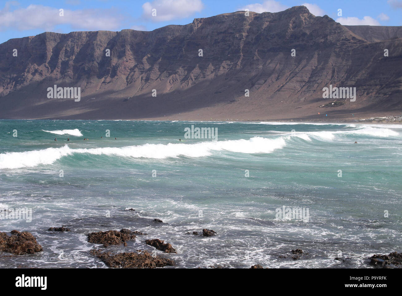 La Caleta de Famara, Lanzarote: Le onde si rotolano sulla riva sotto le torreggianti scogliere vulcaniche, un punto panoramico per il surf sulla selvaggia costa nord-occidentale dell'isola. Foto Stock