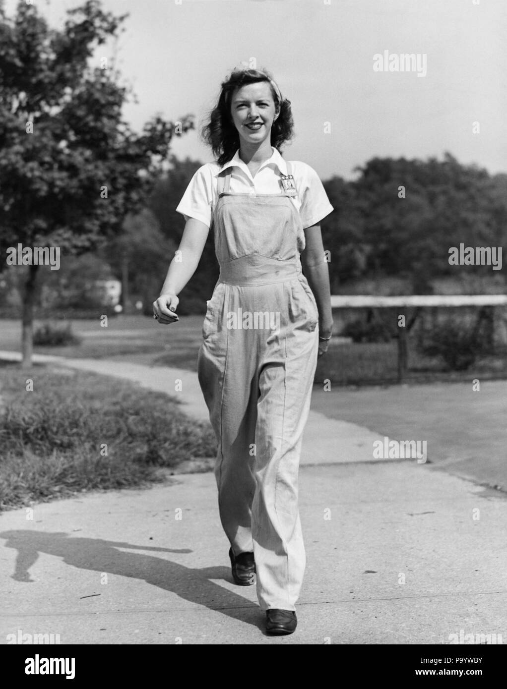 1940s SORRIDENTI DONNA LAVORATRICE OUTDOOR camminare verso indossando tute da BIB TUTE abiti da lavoro guardando la fotocamera - Q43287 CPC001 HARS crescente giovane adulto lieta gioia LIFESTYLE FEMMINE WW2 cresciuto rurale HOME VITA comunicando a tutta lunghezza LADIES FITNESS FISICO DELLE PERSONE TUTE grown-up di fiducia di Agricoltura Agricoltura B&W contatto visivo occupazione allegro forza verso guerre mondiali INDIPENDENTI LA SECONDA GUERRA MONDIALE LA SECONDA GUERRA MONDIALE II GUERRA MONDIALE sorrisi crescere gioiosa Rosie la rivettatrice elegante GUERRA MONDIALE 2 BIB comunicare giovane donna adulta in bianco e nero di etnia caucasica tute in vecchio stile Foto Stock