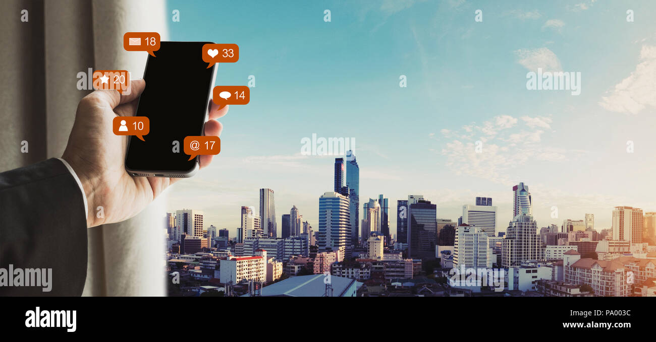 Mano utilizzando mobile smart phone con i social media e social network online e notifica messaggi icone, Bangkok City View Foto Stock