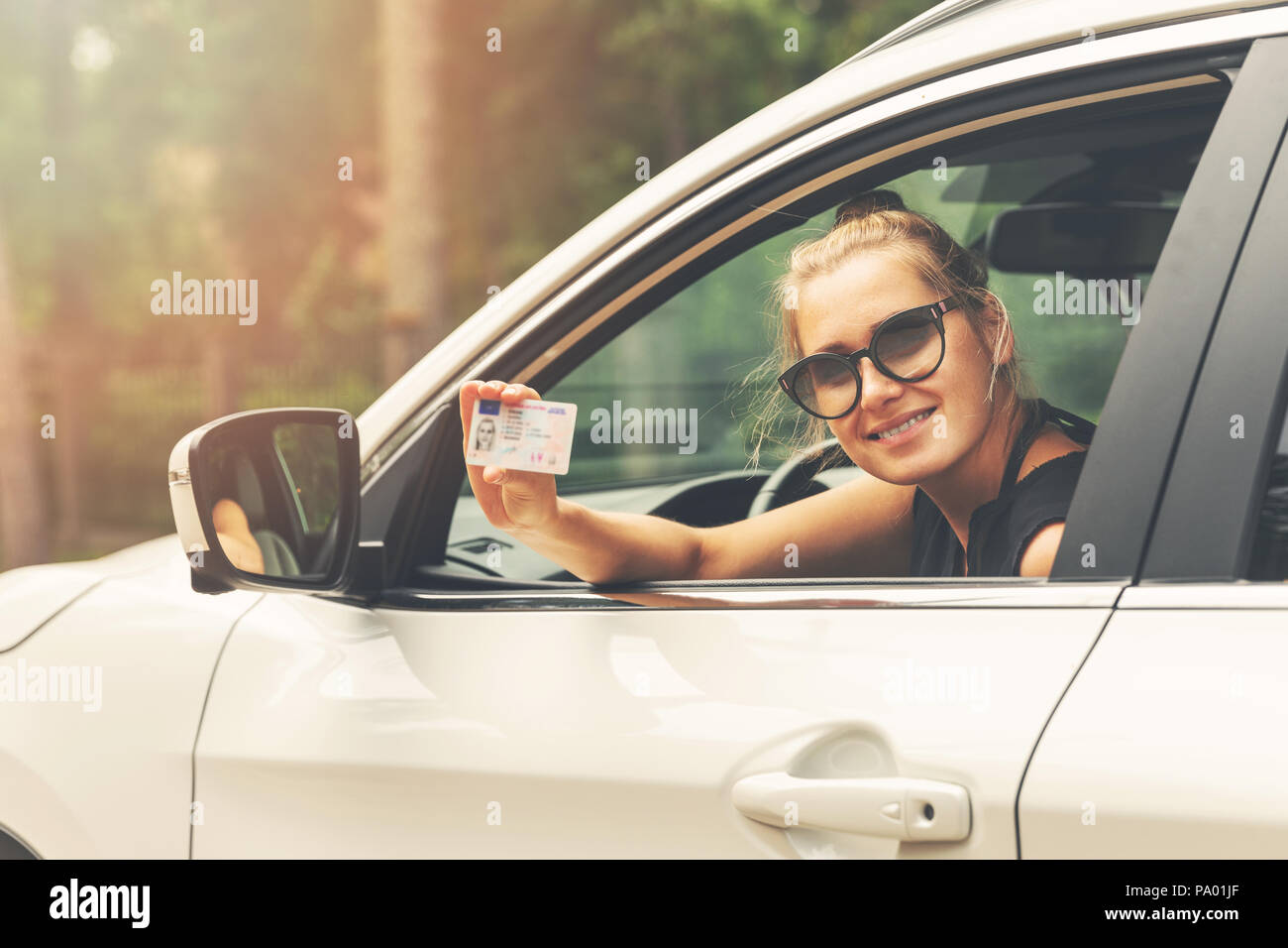 Sorridente donna attraente che mostra la sua licenza di pilota al di fuori della finestra di auto Foto Stock