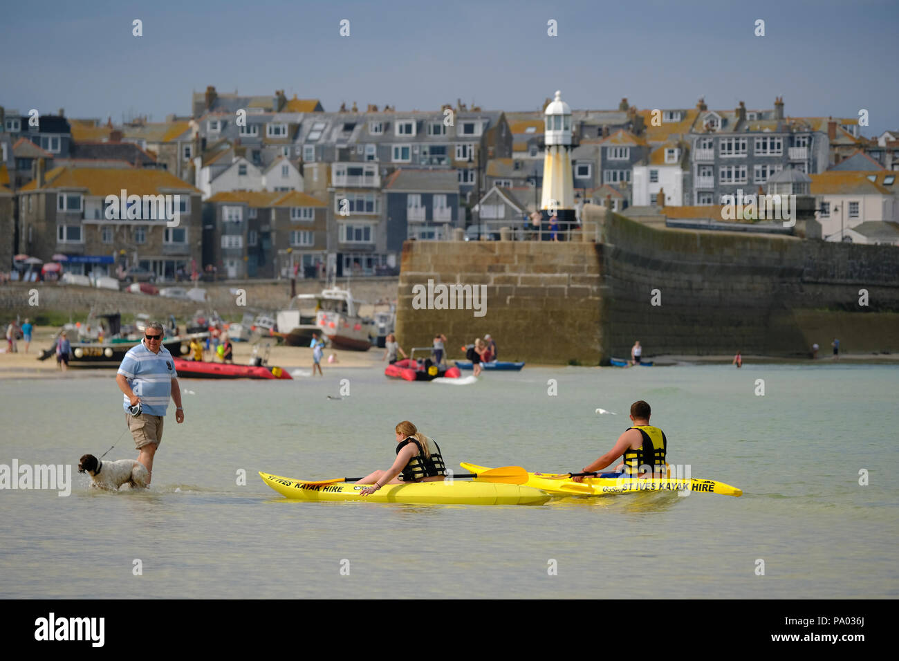 L'uomo con il cane sul piombo sguazzare in acque poco profonde sulla spiaggia di St Ives in Cornovaglia con due giallo kayak nelle vicinanze Foto Stock