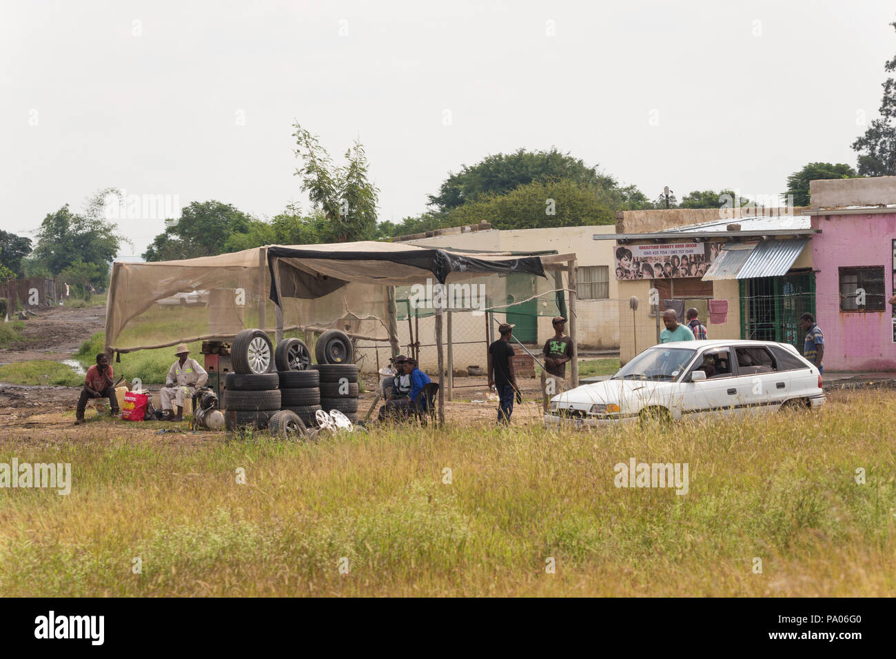 Il montaggio di pneumatici le piccole imprese nelle zone rurali del Sud Africa con gli uomini neri seduti intorno e un auto e gli edifici in background Foto Stock