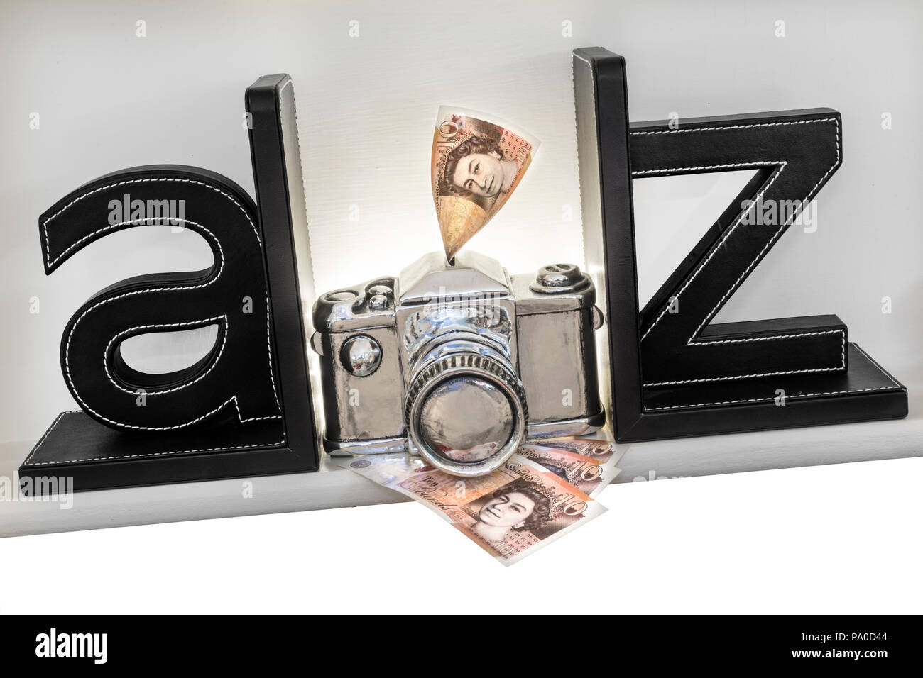 Concetto A-Z 'make denaro dalla tua fotocamera' immagini fotografia che vendono. £10 note andando in risparmio slot nella parte superiore di un concetto di stile fotocamera argento Foto Stock