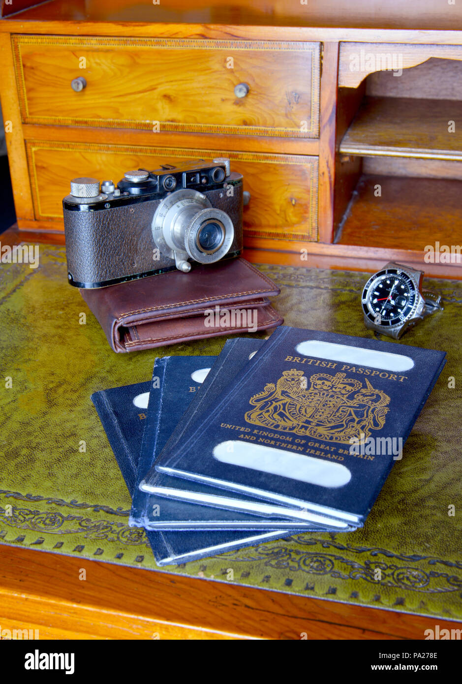 Antica scrivania con passaporti e vecchia leica fotocamera, orologio rolex con nomi tranciati Foto Stock