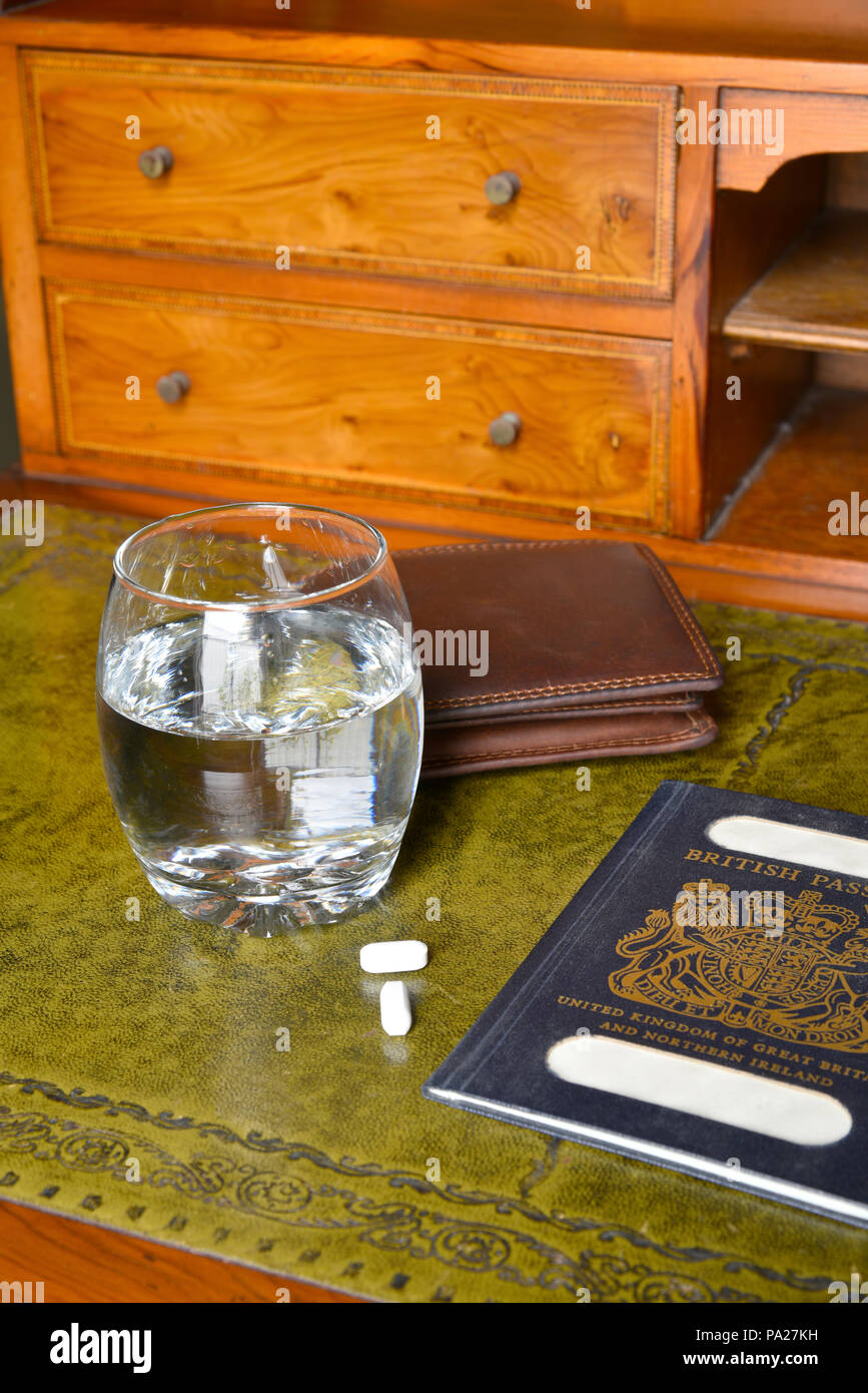 Antica scrivania con passaporti e portafogli e un bicchiere di acqua con le pillole di fianco con nomi tranciati Foto Stock