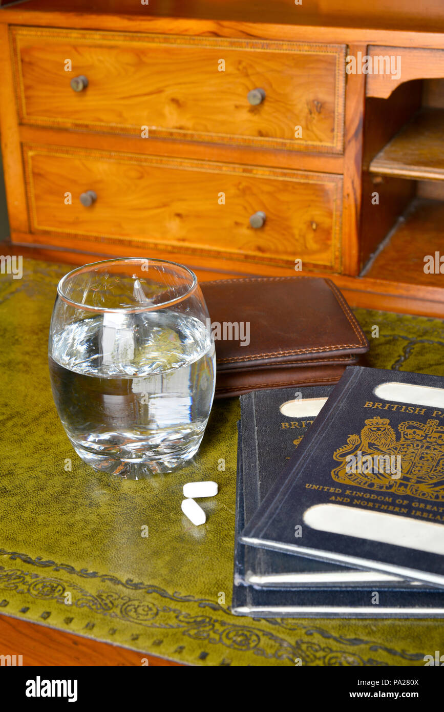 Antica scrivania con passaporti e portafogli e un bicchiere di acqua con le pillole di fianco con nomi tranciati Foto Stock