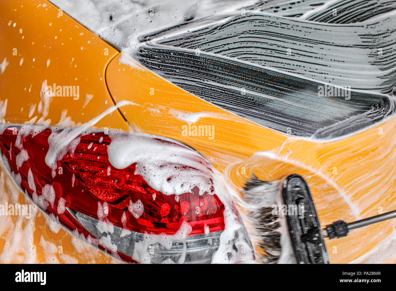 Dettagli sul retro del giallo auto essendo lavato a autolavaggi, spazzola corse di lasciare in bianco la schiuma e shampoo. Foto Stock