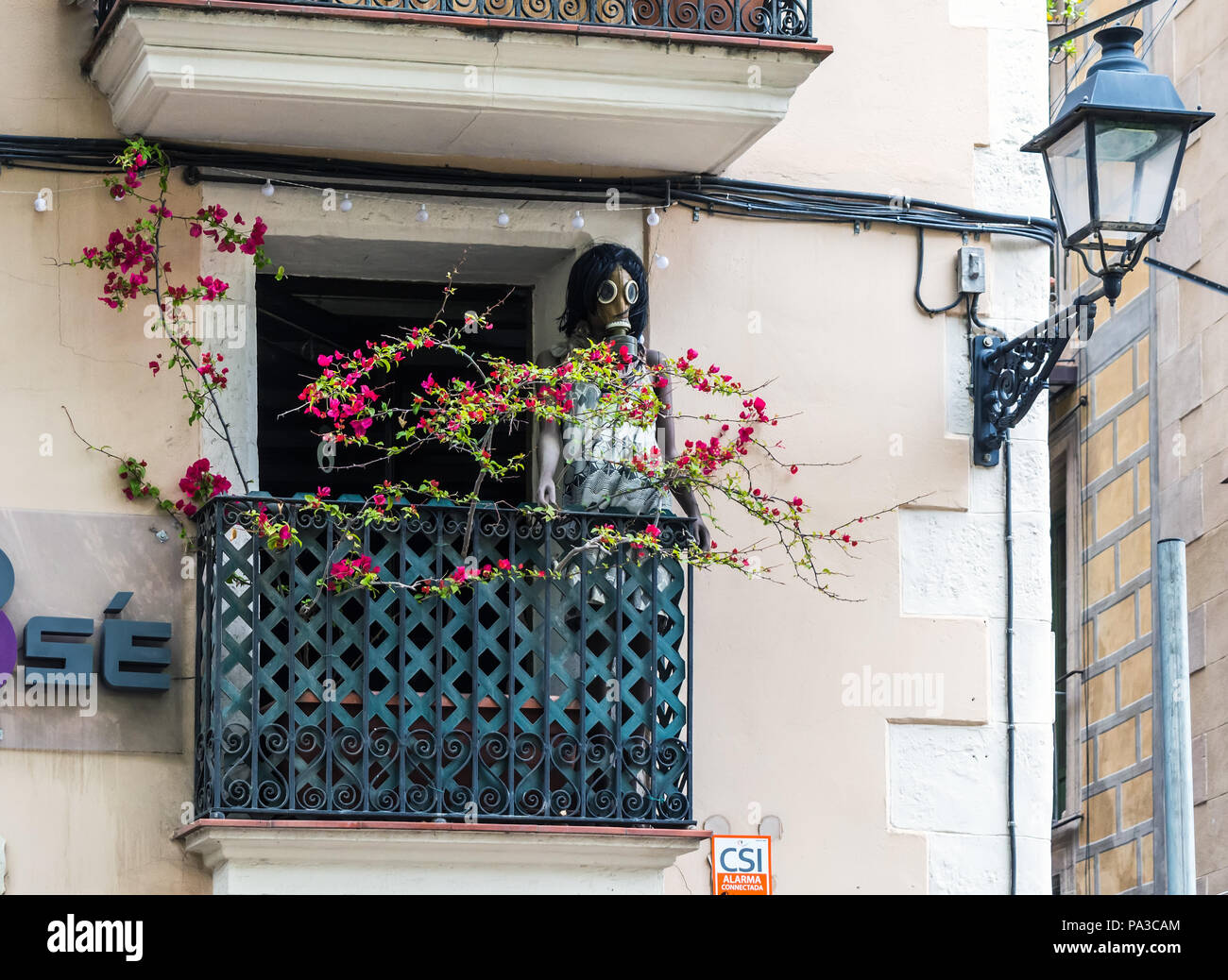 Manichino in abito e maschera a gas permanente sulla normale balcone di Barcellona ritorto con fiori di colore rosso. Foto Stock