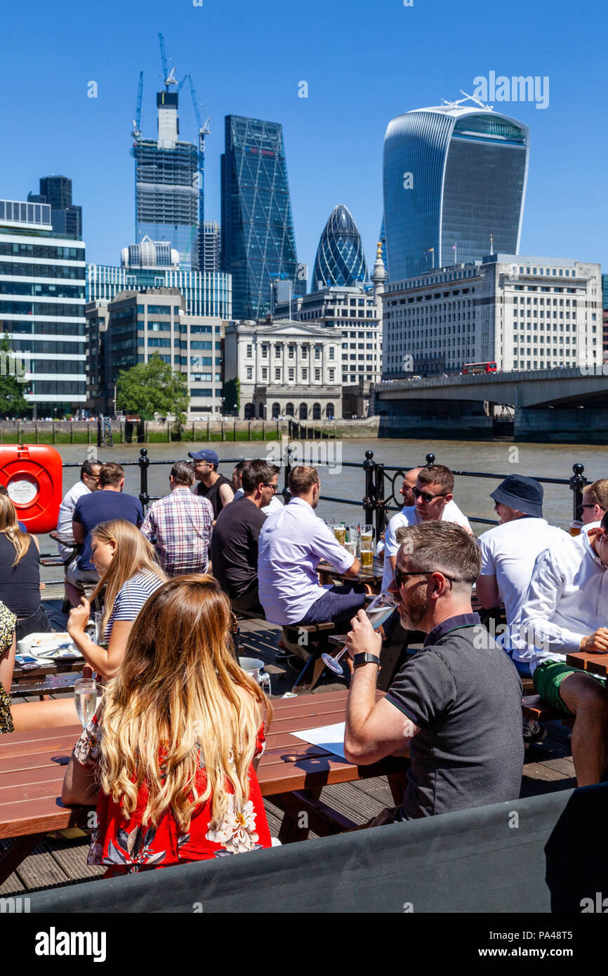 Un gruppo di persone che godono di un ora di pranzo drink presso un pub che si affaccia sul Fiume Tamigi con la City di Londra In Backround, Londra, Inghilterra Foto Stock
