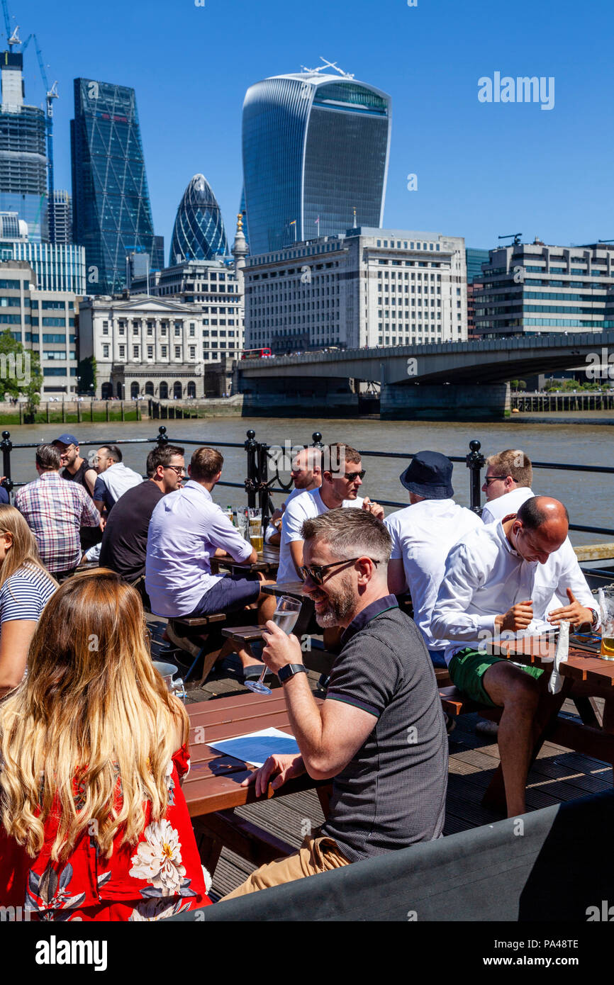 Un gruppo di persone che godono di un ora di pranzo drink presso un pub che si affaccia sul Fiume Tamigi con la City di Londra In Backround, Londra, Inghilterra Foto Stock