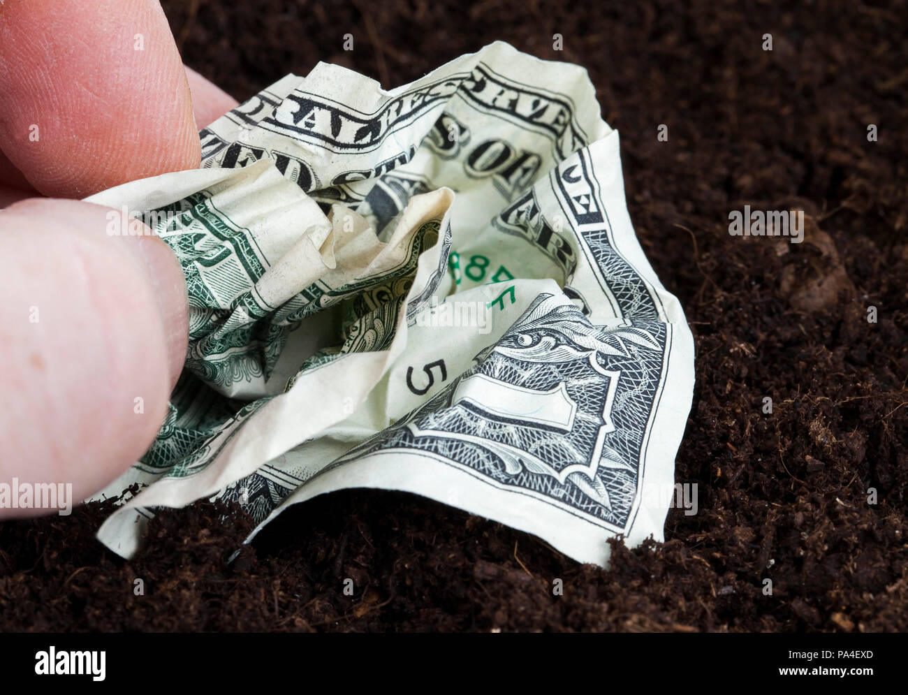 Crumpled un dollaro statunitense in una mano d'uomo contro uno sfondo di colore scuro suolo, primo piano Foto Stock